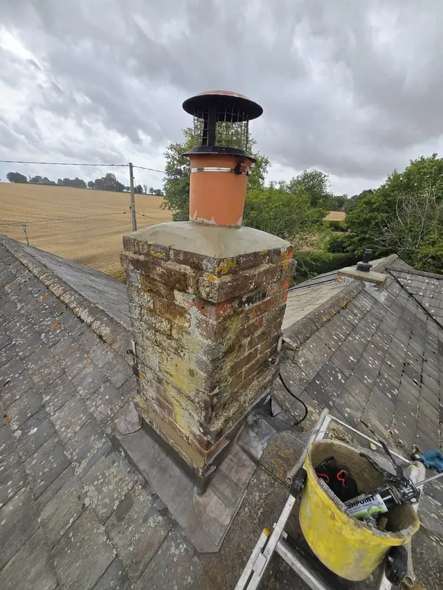 Chimney with a new pot and cowl on a slate roof with fields behind
