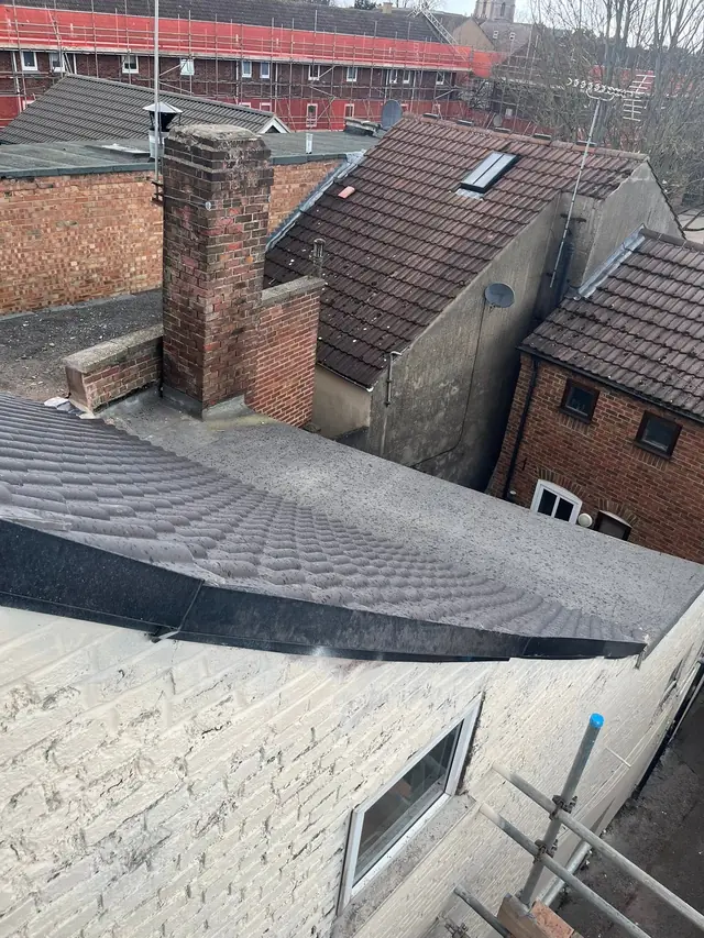 Finished grey flat roof with rooftops and chimneys behind
