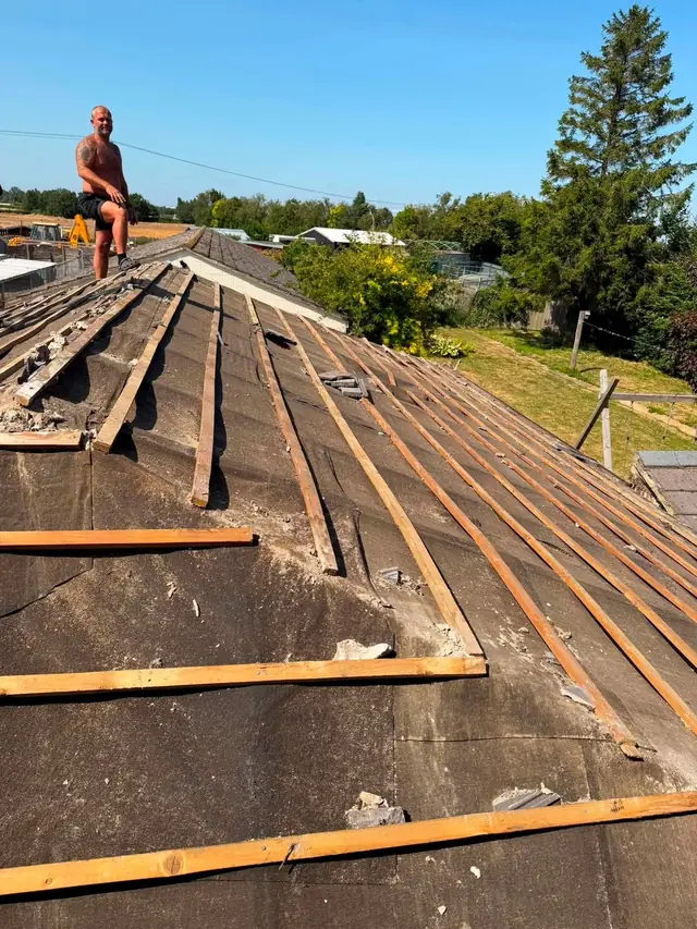 Roofer laying new battens on a fully stripped roof with open fields behind
