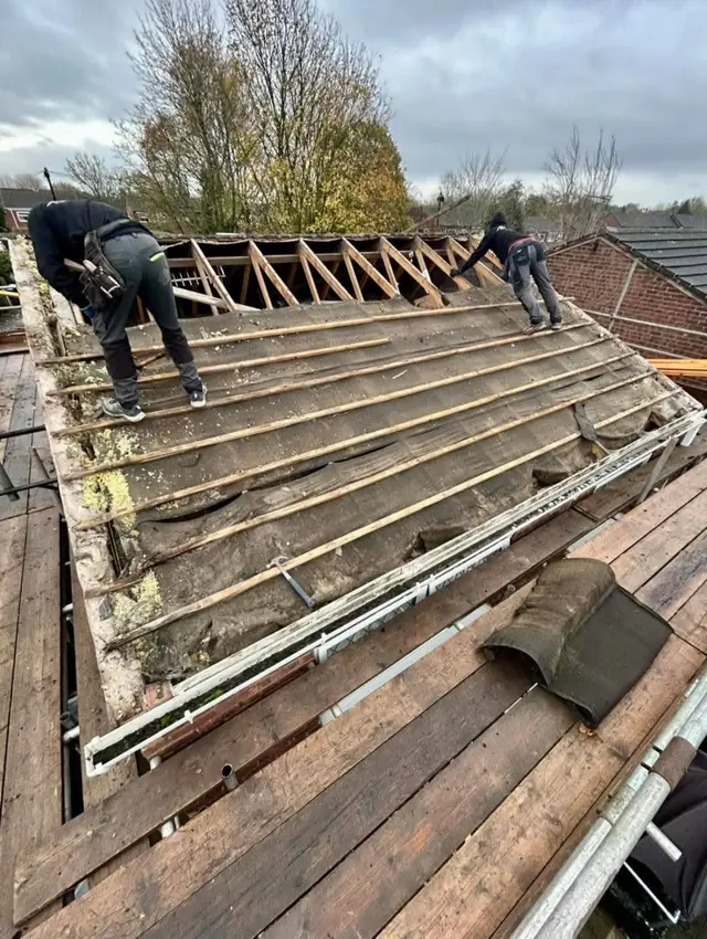 Stripped roof showing new rafters and battens with a roofer at work