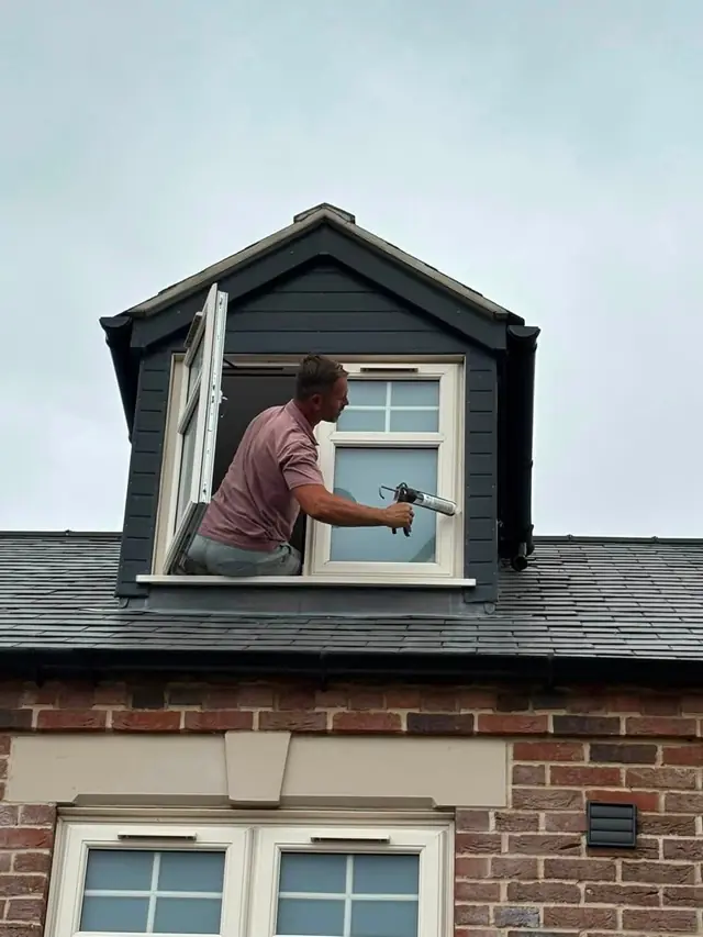 Roofer working at a dormer window on a slate roof